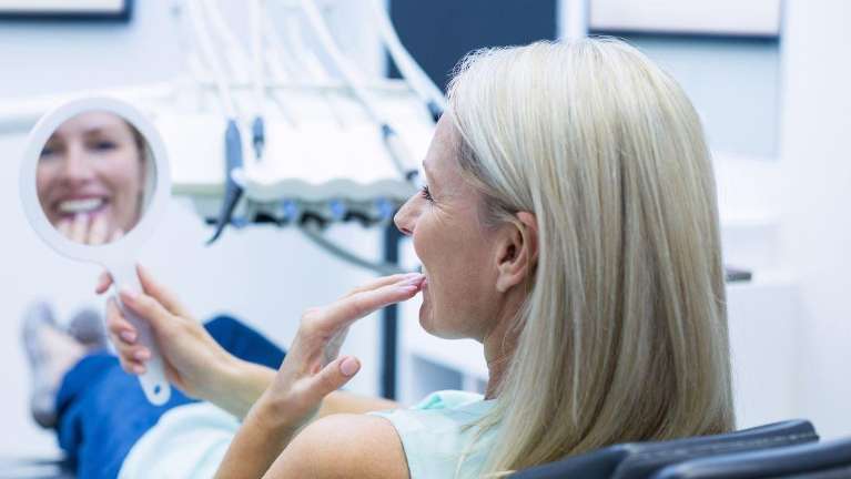 woman sitting in a dental chair while looking at a mirror