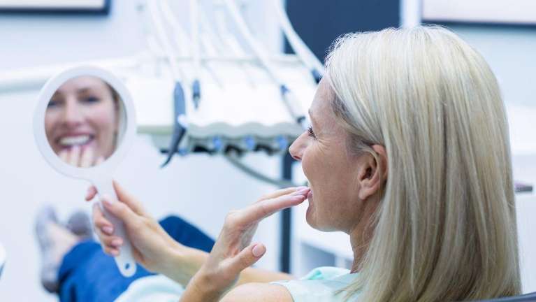 woman sitting in a dental chair while holding a mirror